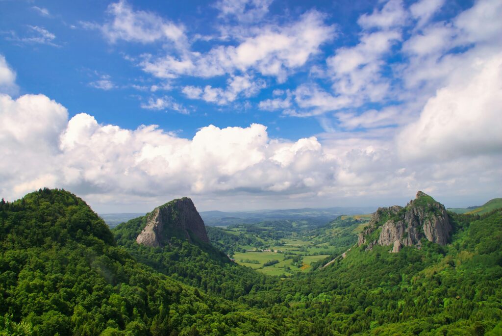A stunning summer view of Roche Sanadoire and Roche Tuiliere with lush greenery under a vibrant blue sky.